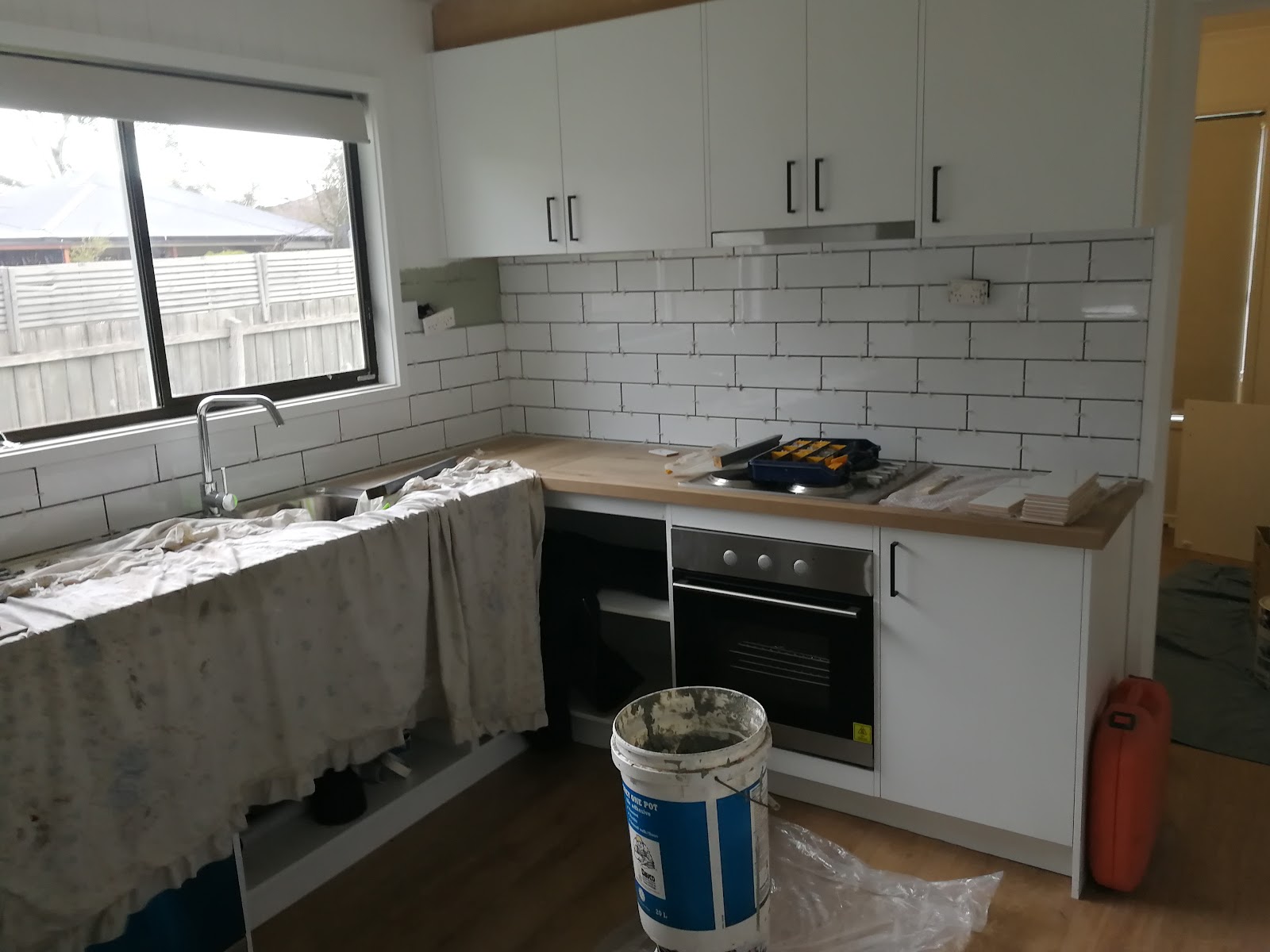 Kitchen mid-renovation: new white cupboards, subway tile splashback and drop sheets